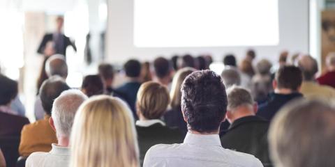 Persone sedute ascoltano una presentazione in sala conferenze.