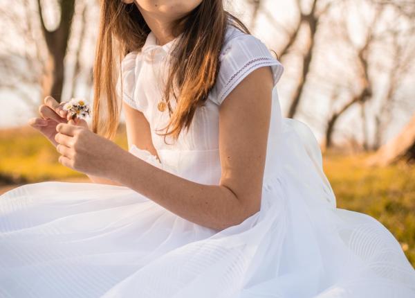 Ragazza in abito bianco con fiori, seduta all'aperto.