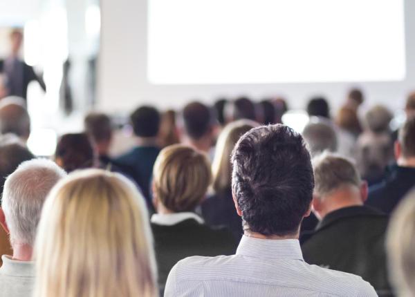 Persone sedute ascoltano una presentazione in sala conferenze.