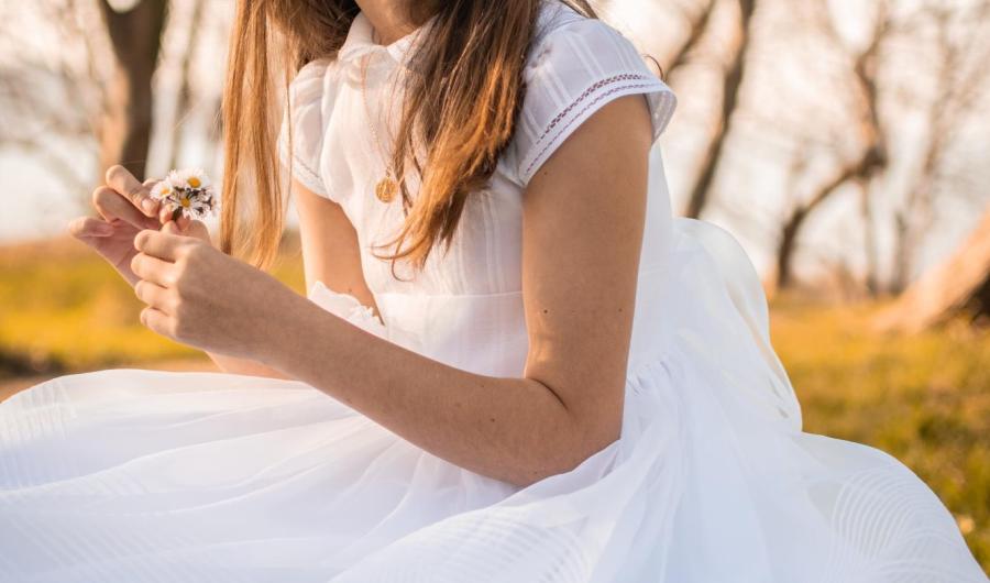 Ragazza in abito bianco con fiori, seduta all'aperto.