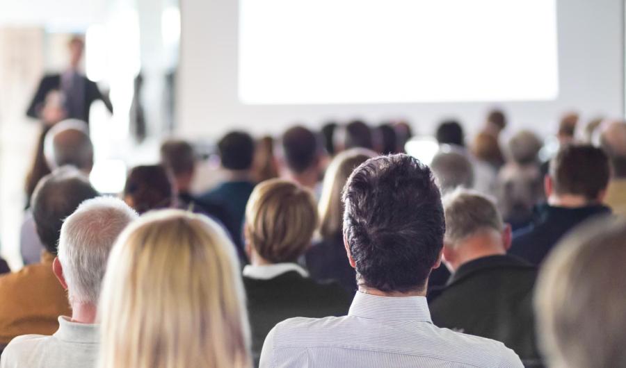 Persone sedute ascoltano una presentazione in sala conferenze.